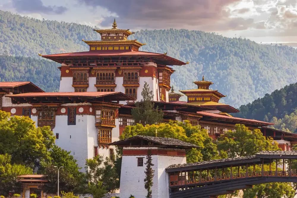 Whitewashed walls, carved windows and tiered roofs of a Bhutanese dzong against forested hills